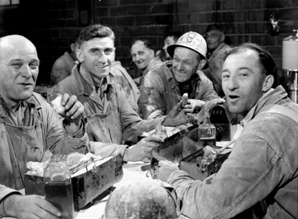 Workers of the Asbestos Corporation enjoying their lunch at lunch tables
                provided by the corporation.