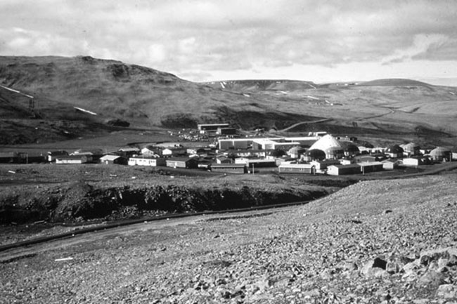 A photograph of Nanisivik townsite circa 1991. The photo is taken from a vantage point higher up on the foothills looking down at the townsite and its many small buildings closely grouped together.