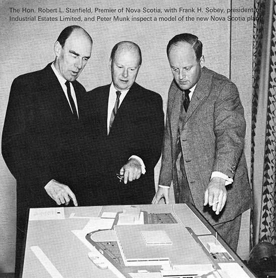 Three men (Robert Stanfield, Frank Sobey, and Peter Munk) stand over and point at a model of the Clairtone Sound plant in Nova Scotia.