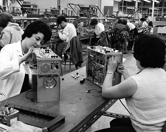 A photograph of women seated and  working on component boxes for stereos at the Clairtone Sound assembly line at Pictou Estates.