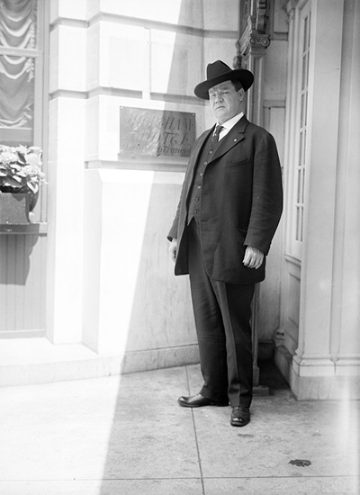 A photo of a middle aged white man wearing a dark suit and hat.