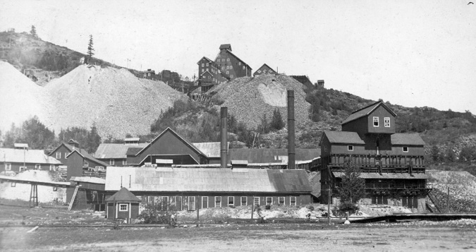 A photo of the Rossland mine. There are numerous buildings with smokestacks and large piles of dirt or rock.