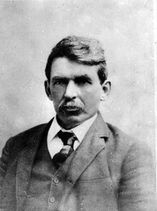 A middle aged white male with a mustache wearing a suit.