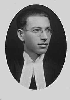 A head shot of a young white man with glasses wearing graduation robes.