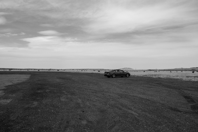 A photograph of a solitary car parked in a vast open area.